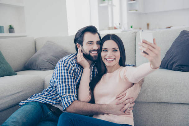 Portrait of lovely positive couple sitting on the floor indoor in house using smart phone shooting self portrait on front camera having video-call fun, enjoying time together - Valokuva, kuva