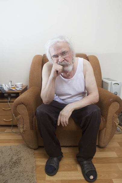 Vanha yksinäinen köyhä mies, joka kärsii silmäsairaudesta kaihi ja glaukooma, istuu tuolissa aivan yksin.
. - Valokuva, kuva