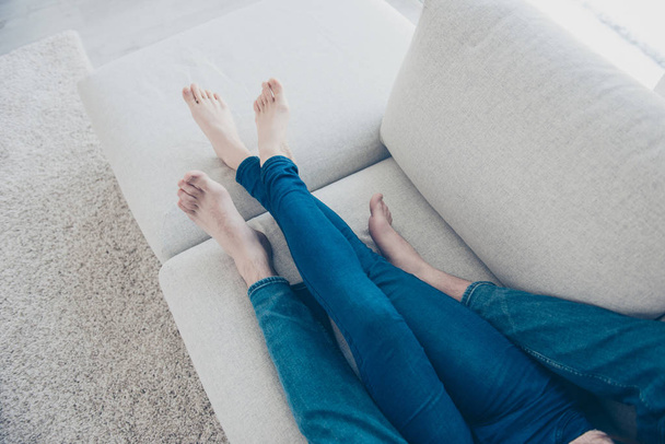 Top view cropped portrait of couples legs in jeans lying on sofa in house apartment, spending time with each other, watching film. Idyllic harmony delight concept - Photo, Image