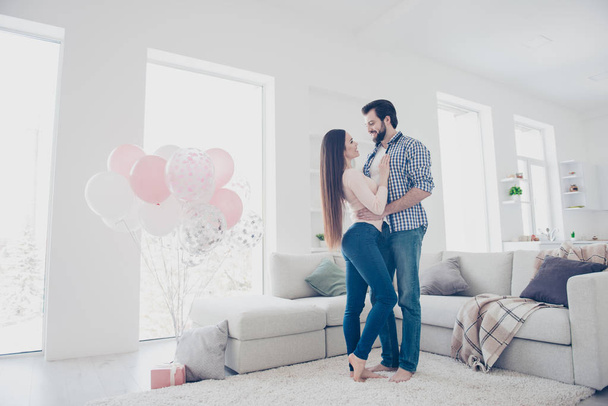 Full length size portrait of lovely romantic couple in casual outfits embracing standing near couch in modern white apartment enjoying holiday having present gift surprise - Foto, immagini