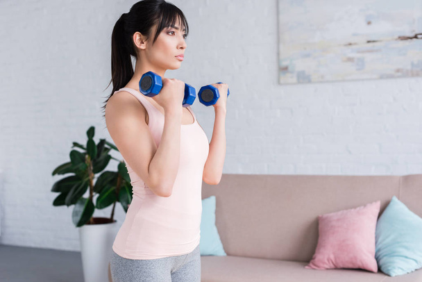 beautiful young sportswoman working out with dumbbells at home - Photo, image