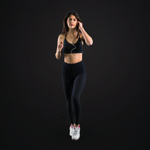 Young sport girl listening music while running on black background - 写真・画像
