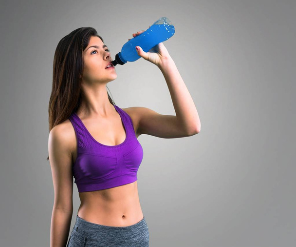 Молода спортивна дівчина з пляшкою на сірому фоні
 - Фото, зображення