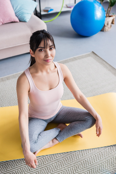 vista ad alto angolo di bella giovane donna seduta su tappetino yoga in posa loto a casa
 - Foto, immagini