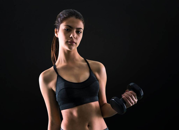 Young sport girl making weightlifting on black background - Photo, Image