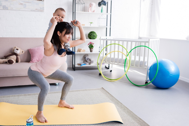 jeune mère sportive portant son petit enfant sur les épaules tout en faisant des squats
 - Photo, image