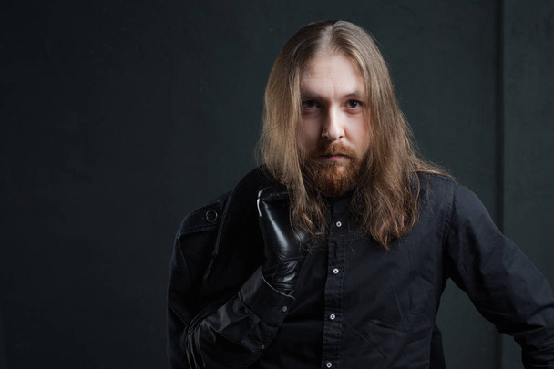 Portrait of man with long hair and beard in black clothes on dark background - Foto, Imagem