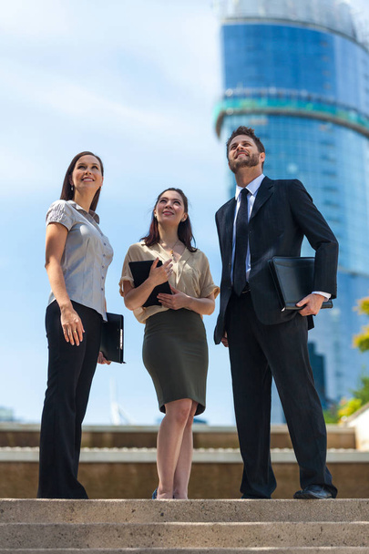 Business team of successful man and women, businessman businesswoman, together looking up to a blue sky in a modern city - Fotó, kép