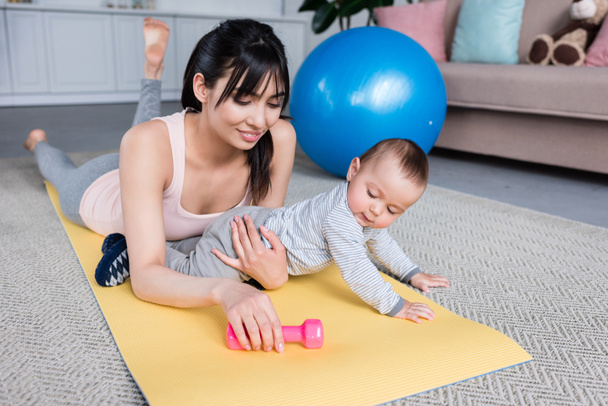 young beautiful mother and little child lying on yoga mat at home together - Fotoğraf, Görsel