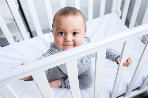 high angle view of adorable little child sitting in baby cot - Zdjęcie, obraz