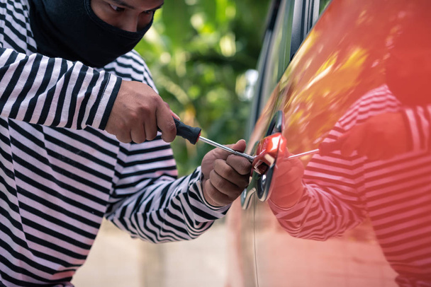 Κλέφτης αυτοκινήτων προσπαθεί να ξεκλειδώσετε ένα αυτοκίνητο με κατσαβίδι. - Φωτογραφία, εικόνα