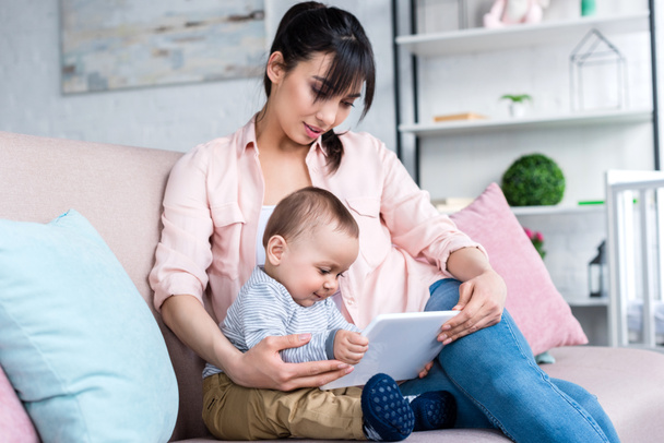 young happy mother and little child with tablet sitting on couch at home - Φωτογραφία, εικόνα