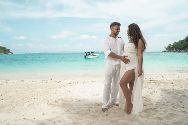 Attractive young couple on the tropical island. Beautiful woman and man wearing white clothes embracing each other and enjoying trpoical holidays vacation getaway - Photo, Image