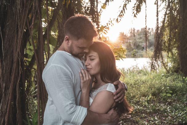 Ελκυστική ρομαντικά νεαρό ζευγάρι στον τροπικό κήπο κατά τη διάρκεια του ηλιοβασιλέματος - Φωτογραφία, εικόνα