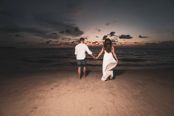 Приваблива романтична молода пара на піщаному тропічному пляжі під час красивого заходу сонця
 - Фото, зображення