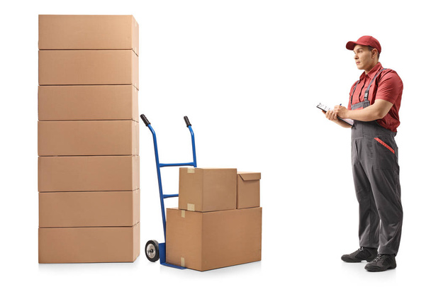 Full length profile shot of a mover looking at stacks of boxes and writing in clipboard isolated on white background - Фото, зображення