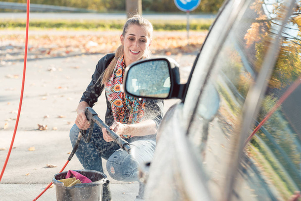 Γυναίκα που χρησιμοποιούν υψηλή πίεση ακροφυσίων για να καθαρίσετε το αυτοκίνητό της - Φωτογραφία, εικόνα