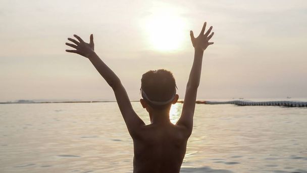 Aziatische jongen verhogen zijn handen omhoog in de lucht op het strand. - Foto, afbeelding