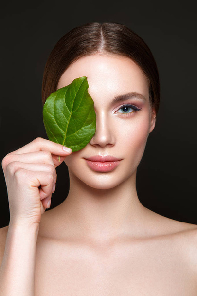 Beautiful woman portrait on black background with clean skin and green leaf in hand. - Foto, imagen