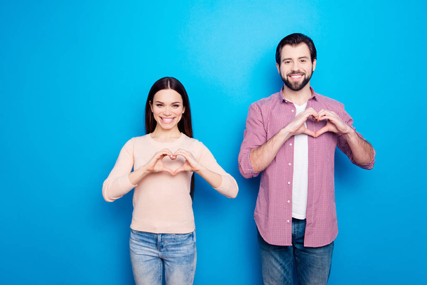 Portrait of cheerful joyful partners in casual outfits jeans showing heart figure love signs with fingers looking at camera isolated on vivid blue background - Photo, image