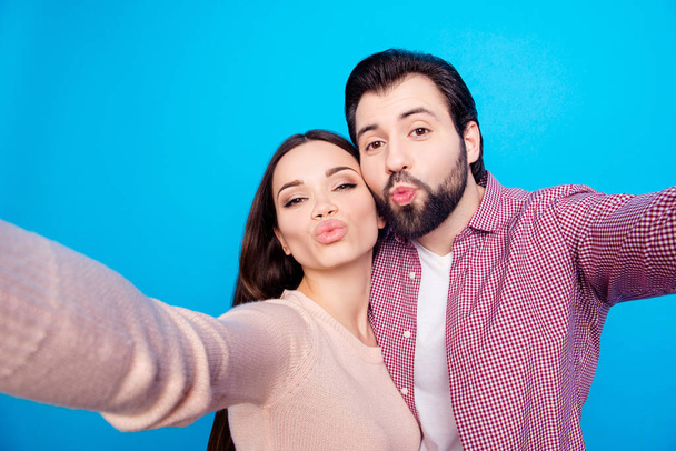 Self portrait of trendy lovely couple shooting selfie on front camera sending kisses with pout lips isolated on blue background. Rest relax valentine day concept - Фото, зображення