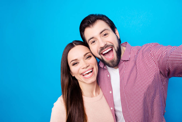 Self portrait of toothy lucky partners with beaming smiles shooting selfie on front camera isolated on vivid blue background - Фото, зображення
