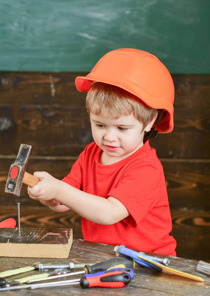 Veiligheid op de werkplek. Klein kind in oranje helm hameren nagels. Leuke jongen spelen met hulpmiddelen - Foto, afbeelding