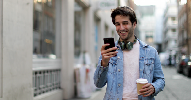 Young adult male walking down street looking at smartphone - Filmagem, Vídeo