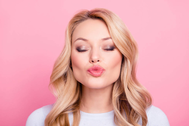 Portrait of lovely sweet girl in casual outfit with modern hairdo sending blowing kiss to the camera with close eyes isolated on pink background. Affection feelings concept - Фото, зображення