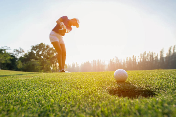 Golfer asian woman focus putting golf ball on the green golf on sun set evening time.. Healthy and Lifestyle Concept - 写真・画像