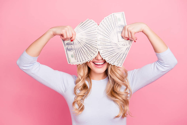 Portrait of crazy playful foolish girl with beaming smile holding fans from much money in hands cover her eyes isolated on pink background - Фото, зображення