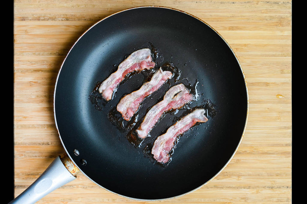 slices of fresh fried bacon in a pan for breakfast on a black background - Fotoğraf, Görsel