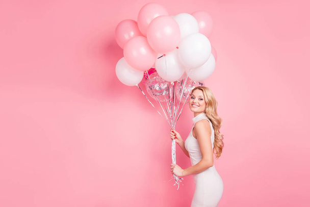 Side view portrait of sexy stunning girlfriend having many colorful air ballons in hands looking at camera isolated on pink background with copy space - 写真・画像