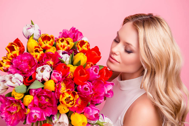 Portrait of lovely cute wife, charming girlfriend, mother with close eyes enjoying smell of aromatic fresh big bouquet of tulips isolated on pink background - Fotó, kép