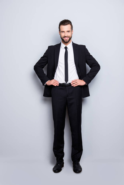 Full size fullbody portrait of cheerful attractive business person wearing black suit with tie looking at camera, holding hands on waist, isolated on grey background - Fotoğraf, Görsel