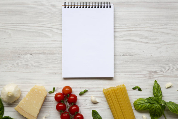 Σημειωματάριο με συστατικά για το μαγείρεμα των ιταλικών ζυμαρικών σε λευκό φόντο ξύλινη. Επίπεδη θέσει. Το Top view. Χώρο αντίγραφο - Φωτογραφία, εικόνα