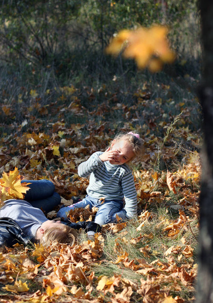 Mladá blondýnka s roztomilá holčička jsou na žluté listí na zemi venku - Fotografie, Obrázek