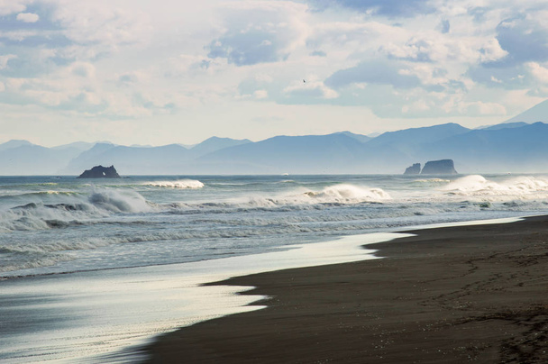 Praia Halaktyr. Kamchatka. Federação Russa. Praia de areia de cor quase negra escura do Oceano Pacífico. Montanhas de pedra e grama amarela estão em um fundo. Céu azul claro
 - Foto, Imagem