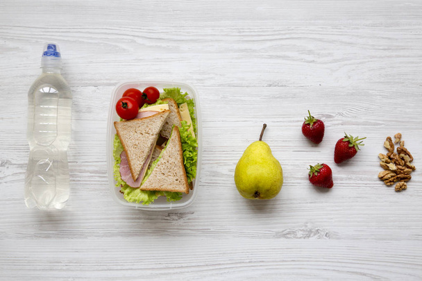 Almoço escolar saudável com legumes orgânicos frescos sanduíches, nozes, frutas e garrafa de água na superfície de madeira branca, vista superior. Deitado. De cima
. - Foto, Imagem