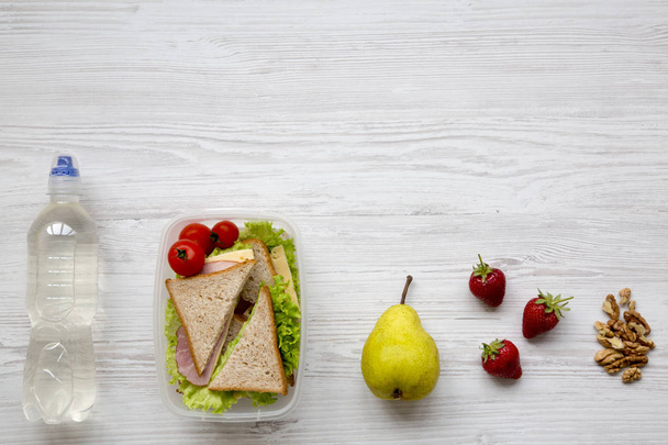 Sağlıklı okul öğle yemeği kutusu taze organik sebze sandviç, ceviz, meyve ve şişe su beyaz ahşap zemin üzerinde düz yatıyordu. Yukarıdan. Kopya alanı. - Fotoğraf, Görsel