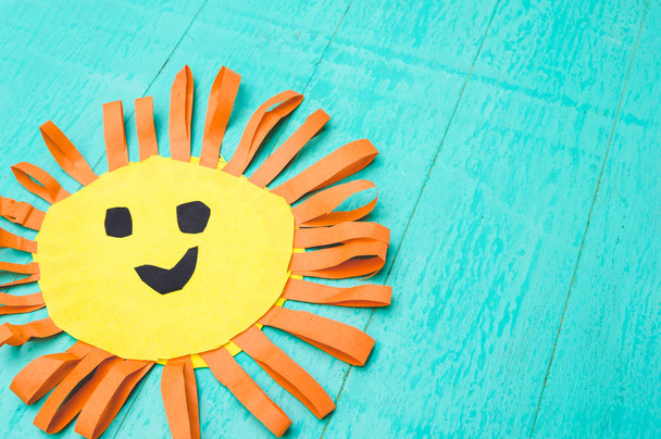 Kinderhandarbeit aus buntem Papier - die Sonne mit einem Lächeln auf blauem Hintergrund - Foto, Bild