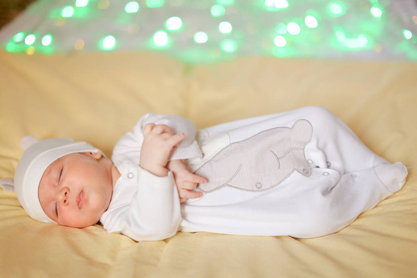 Маленький ребенок в белой кепке лежит на одеяле, зеленые взгляды на заднем плане
. - Фото, изображение