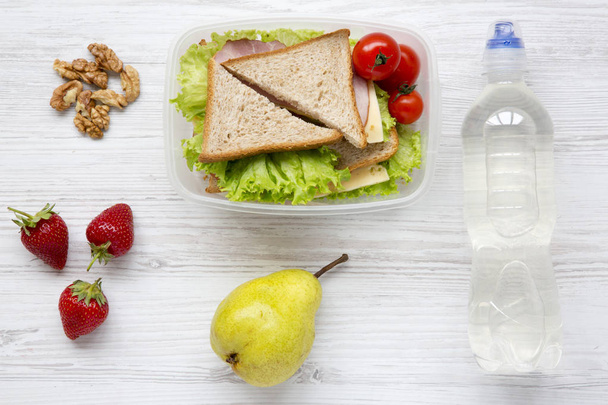 Almuerzo con sándwiches, nueces, botella de agua y frutas en mesa de madera blanca, vista superior. Desde arriba. Puesta plana
. - Foto, Imagen