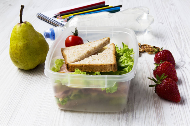 Almoço escolar saudável com caderno e lápis de cor sobre fundo de madeira branca. Vista lateral. Fechar.
. - Foto, Imagem