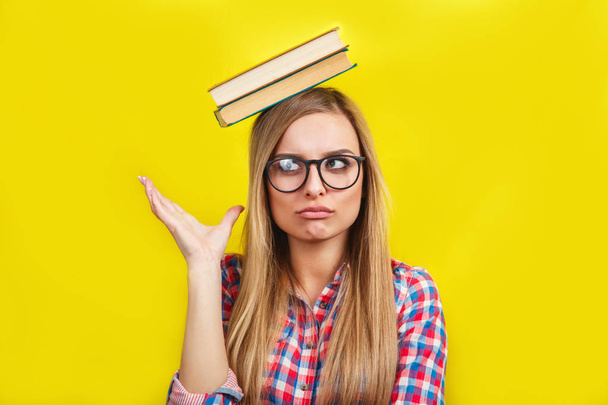 young woman in glasses holding books on her head. Smiling young stylish student is standing with books on yellow background - Foto, immagini