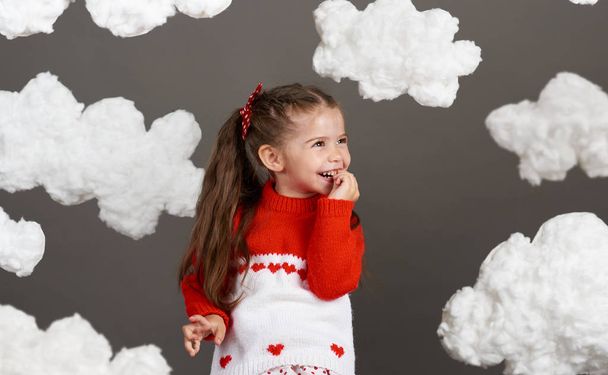 girl playing with clouds, dressed in red sweater, shot in the studio on a gray background - Фото, зображення