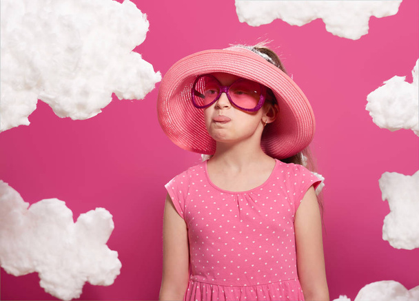divatos lány pózol egy rózsaszín háttér, felhők, rózsaszín ruha és kalap - Fotó, kép