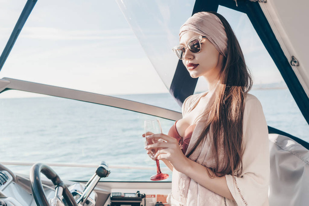 a rich young woman in sunglasses posing on her yacht, drinking champagne and enjoying a vacation - Фото, зображення