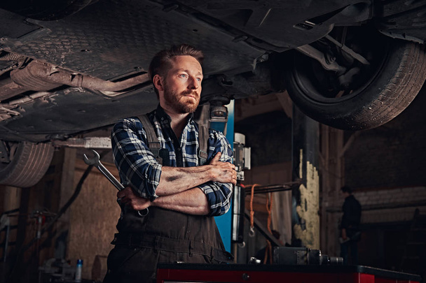 Szerelő keresztbe keze alatt emelési autó javítási garázsban állva. - Fotó, kép