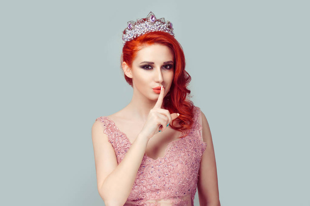 Shh Secret Serious Beauty queen woman actress miss asking for silence secrecy hand gesture light green background. Pretty redheadgirl with crown placing finger on lips hush sign symbol Neutral emotion - Photo, Image